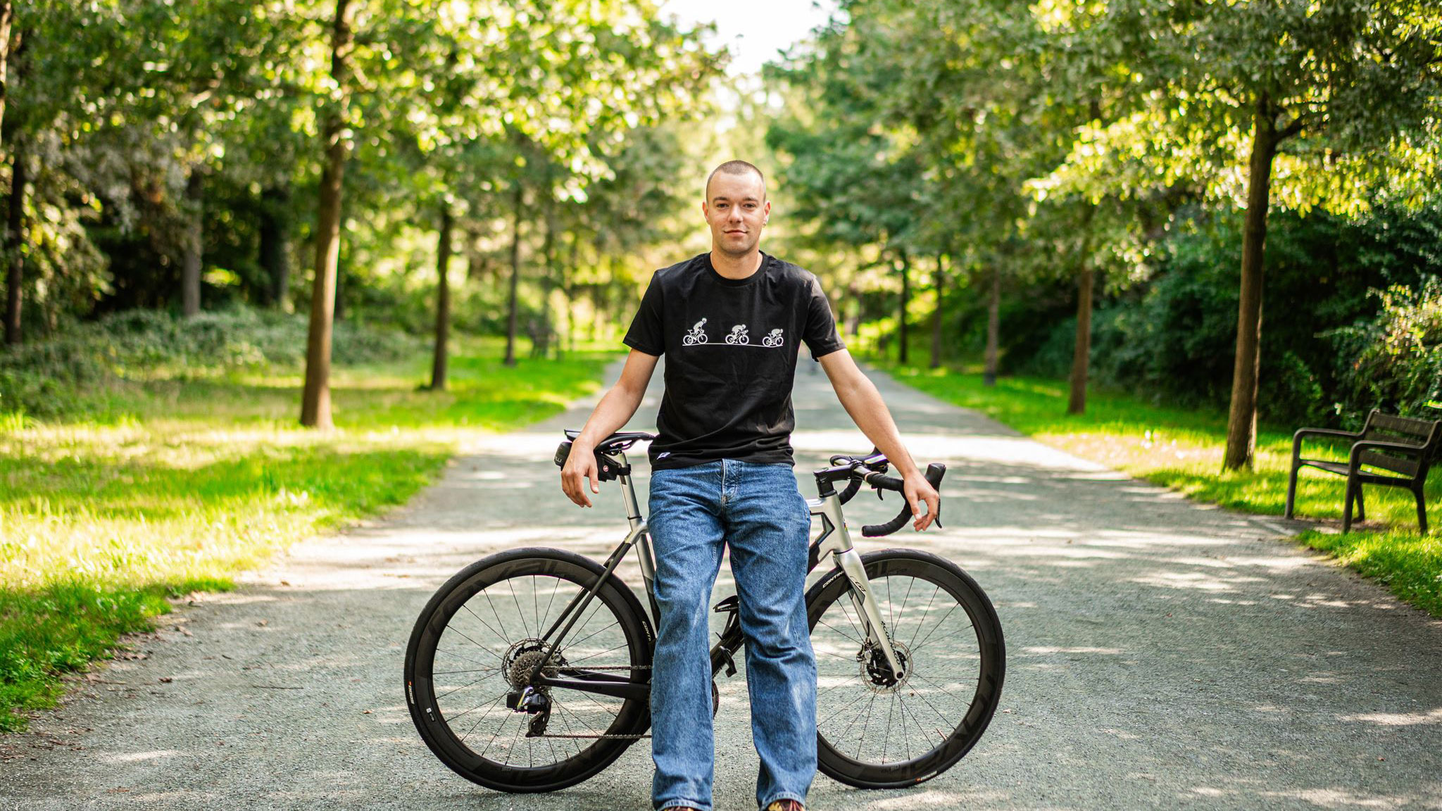 Man leaning on a bicycle, while wearing a cycling shirt.