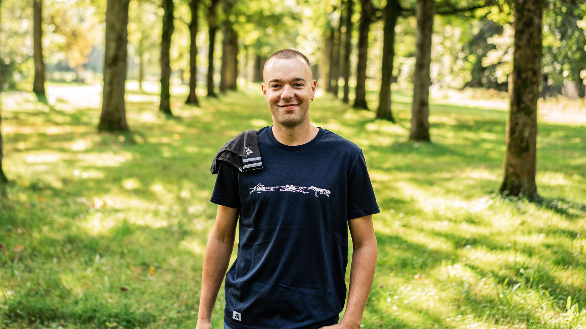 Man with swimsuit over his shoulder wearing a casual T-shirt with a swimming illustration.