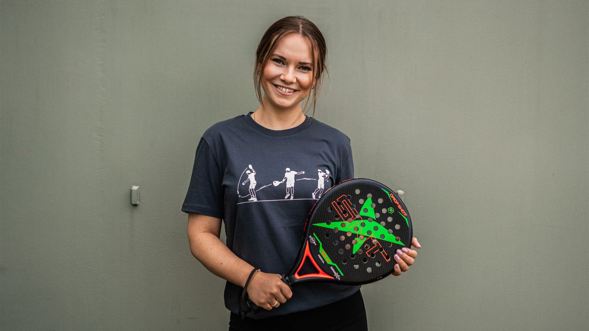 Woman with a padel racket wearing a grey T-shirt with a padel drawing